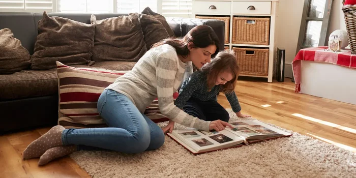 Mutter und Tochter sitzen gemeinsam auf dem Wohnzimmerteppich und schauen ein Fotoalbum an