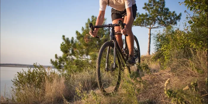 Ein Fahrradfahrer fährt im Gelände mit einem Crossbike bergab. Neben einem See befinden sich auch verschiedene Pflanzen im Hintergrund