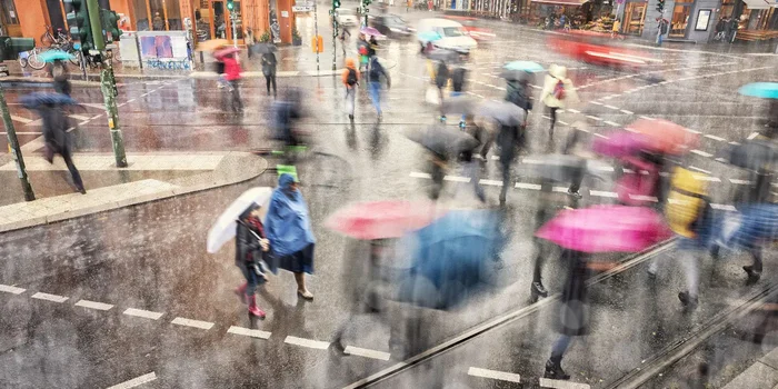 Menschen mit Regenschirmen laufen bei Regen über eine belebte Kreuzung