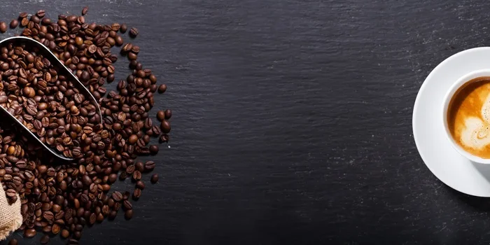 Neben einem Sack mit Kaffeebohnen befindet sich eine Kaffeetasse mit hellem Kaffee