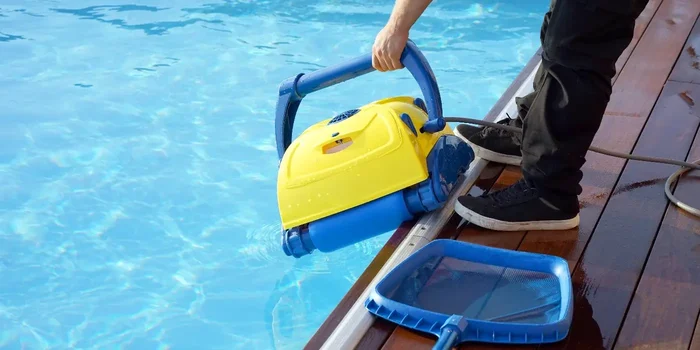 Aufnahme eines gelb-blauen Poolsaugers, der von einer Person in einen Pool eingelassen wird