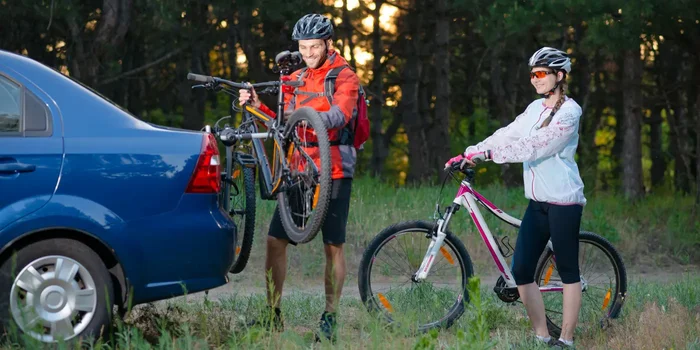 Ein Mountainbiker bringt sein Fahrrad am Fahrradträger eines blauen Autos an, während eine weitere Mountainbikerin zusieht