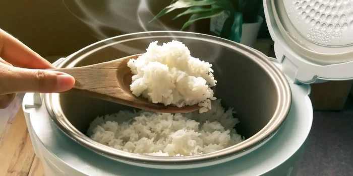 Person entnimmt Reis aus einem Reiskocher mithilfe eines Holzlöffels