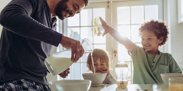 Elternteil schenkt Kind am Frühstückstisch Milch ein
