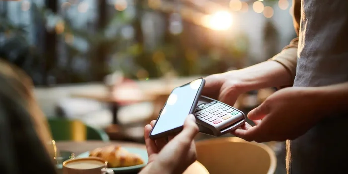 Person hält NFC-Smartphone an ein EC-Kartenlesegerät, um zu bezahlen