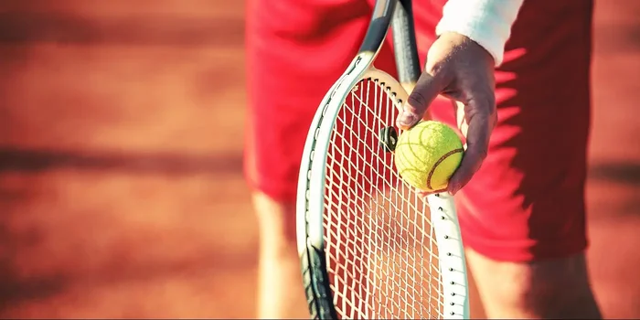 Person hält Tennisball an seinen Schläger zum Aufschlag