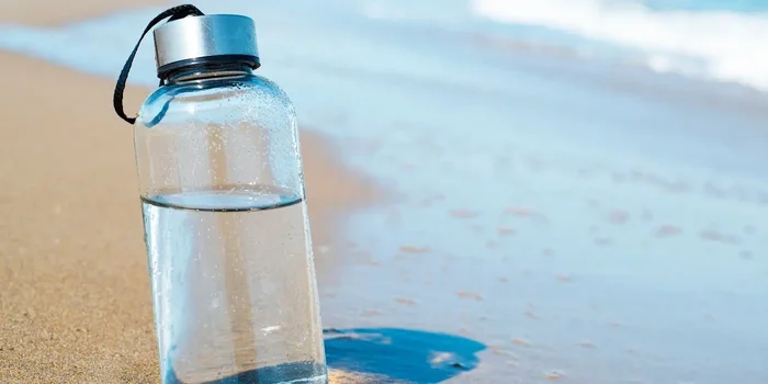 Durchsichtige Trinkflasche steht im Sand am Strand