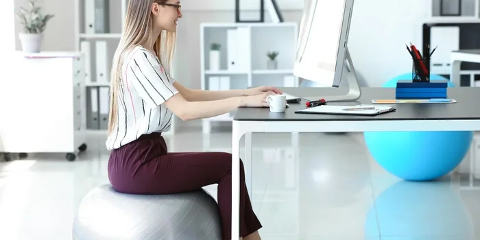 Eine junge Frau sitzt auf einem Gymnastikball an einem Schreibtisch und arbeitet an einem Computer