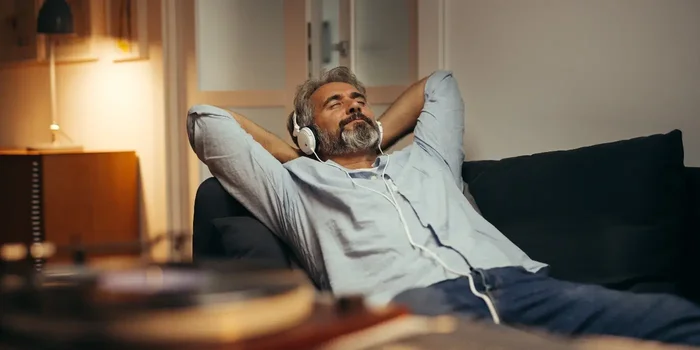 Person mit Kopfhörern auf der Couch und lächelt entspannt