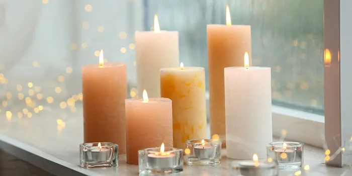Aufnahme verschiedener, heller Kerzen in unterschiedlichen Größen auf einer Fensterbank