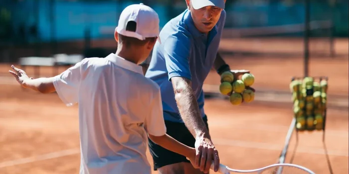 Tennistrainer korrigiert Schlägerhaltung von Schüler