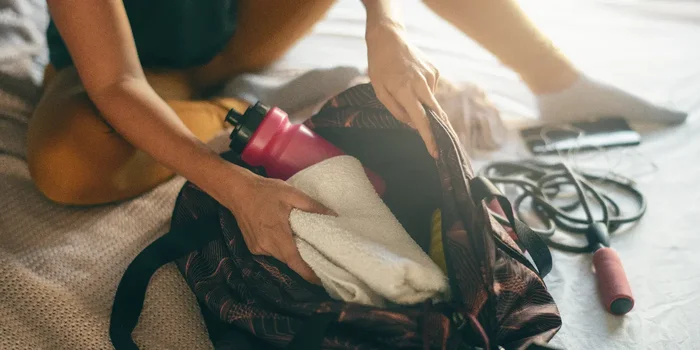 Frau packt Sporttasche für Fitnesstudio mit Trinkflasche und Handtuch