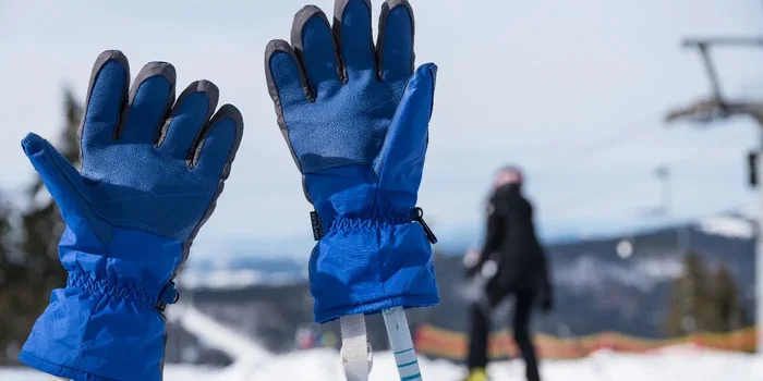 Zwei dicke, blaue Skihandschuhe stecken auf den Griffen zweier Skistöcke im Schnee