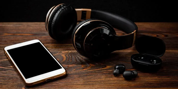 True-Wireless-, Over-Ear-Bluetooth Kopfhörer und Smartphone liegen auf einem Holztisch
