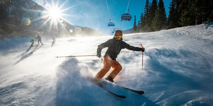 Ein Skifahrer in voller Ausüstung bremst im Schnee ab, sodass Schnee aufgewirbelt wird