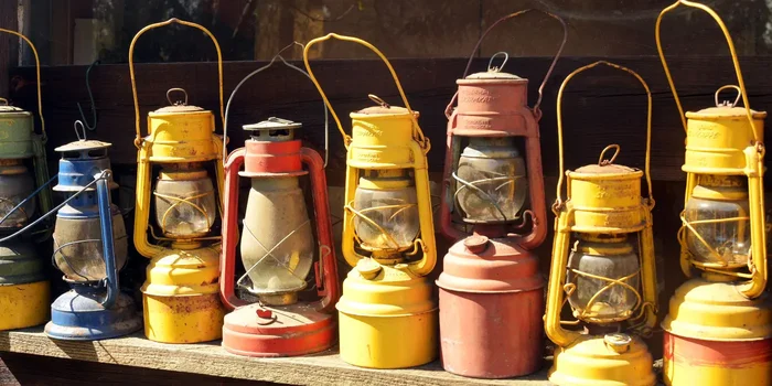 Eine Reihe antiker Petroleumlampen in Rot, Orange und Gelb steht auf einem Regal
