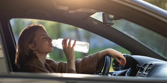 Person am Steuer eines Autos trinkt aus einer Flasche