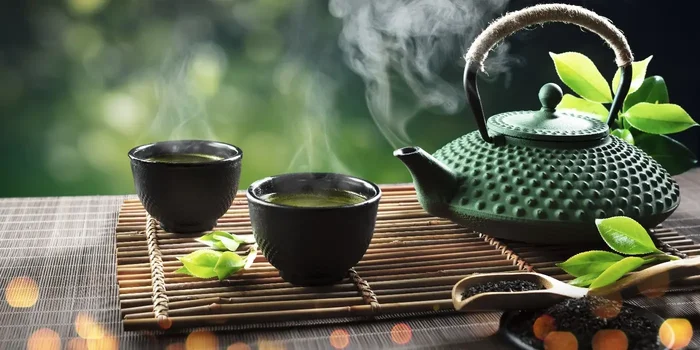 Japanische Teekanne und Teeschälchen mit grünem Tee stehen auf einer Bambusunterlage