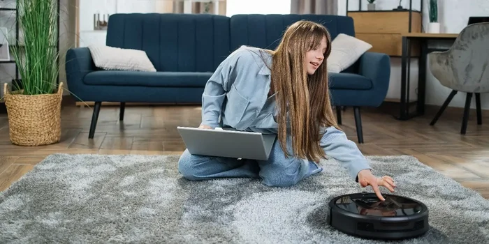 Model sitzt auf dem Wohnzimmerboden und programmiert einen Saugroboter