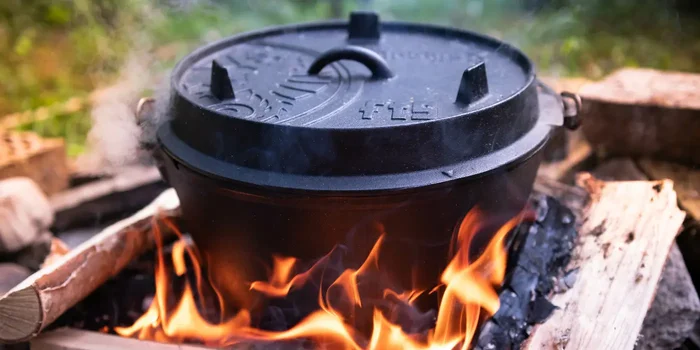 Ein schwarzer Feuertopf aus Gusseisen mit Deckel steht in einer Feuerstelle