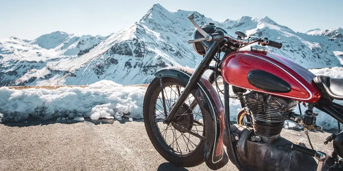 Ein rotes Motorrad parkt vor einer sonnigen, verschneiten Berglandschaft
