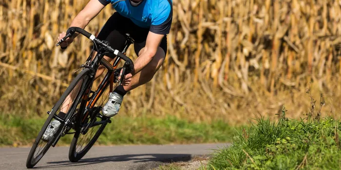Aufnahme eines sportlich gekleideten Radfahrers auf einem Rennrad in einer Kurve vor einem Maisfeld