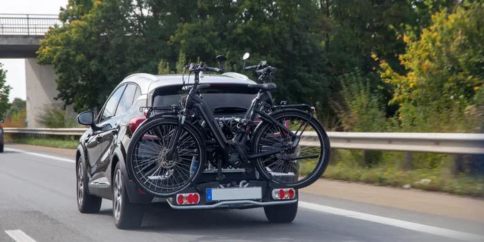 Ein schwarzes Auto mit zwei Fahrrädern auf einem Fahrradträger ist auf der Straße von hinten zu sehen