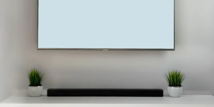 Eine Soundbar steht unter einem hängenden Smart TV auf einem Low Board