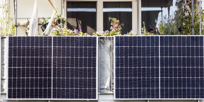 Zwei Solarpanels sind am Geländer eines weißen Balkons mit Grünpflanzen angebracht