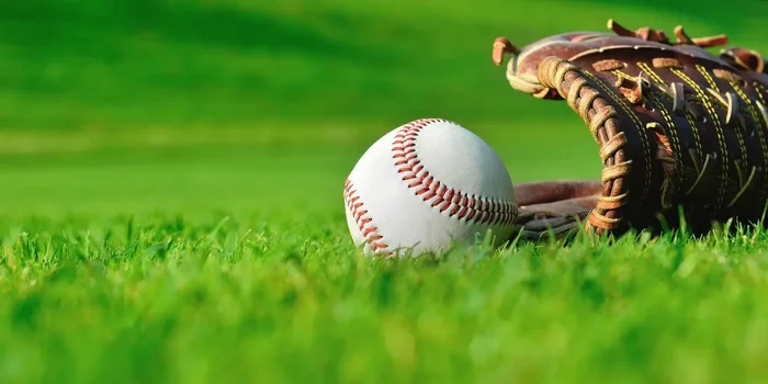 Ein brauner Baseballhandschuh liegt neben einem Baseball auf einer Rasenfläche