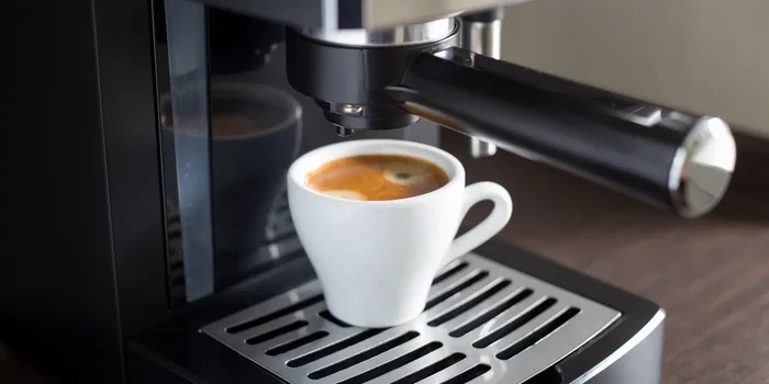 Nahaufnahme eines Kaffeeautomatens, unter dem eine kleine, weiße Tasse mit frisch gebrühtem Kaffee steht