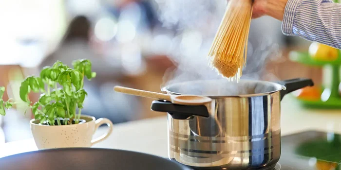 Hand hält Spaghetti über dampfenden Kochtopf in Küche