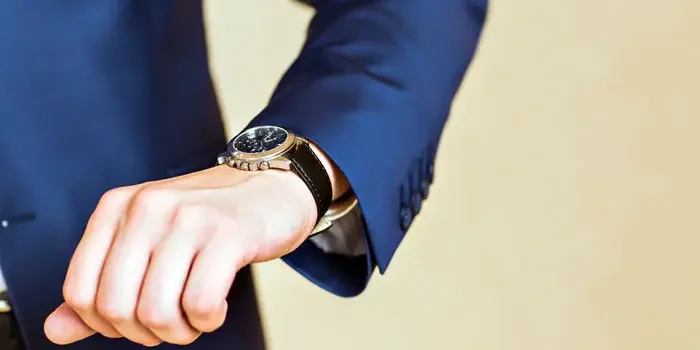 Nahaufnahme einer eleganten Armbanduhr, welche sich am Handgelenk eines Anzugträgers befindet.