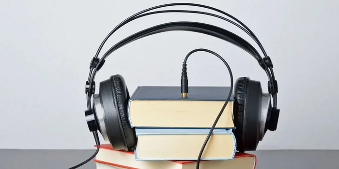 Vier übereinander gestapelte Bücher werden von einem schwarzen Kopfhörer mit Kabel umgeben