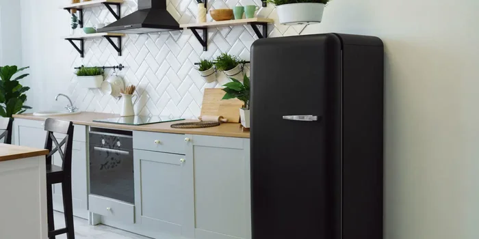 Schwarzer Retro-Kühlschrank steht in grau-weißer Küche mit schwarzen Elementen