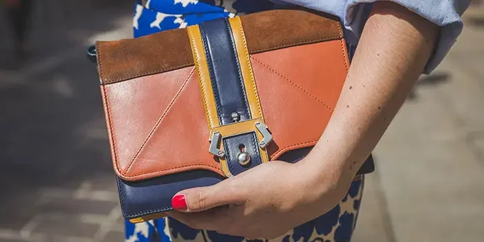 Frau mit roten Fingernägeln hält eine Designerhandtasche