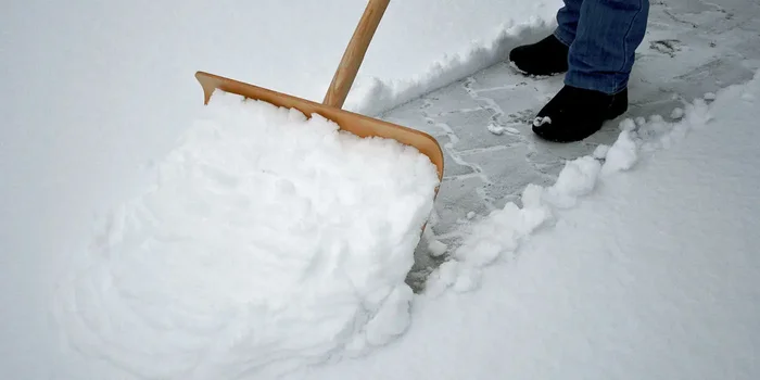 Ein Mann schippt den Schnee mit einem Holzschneeschieber von seinem Weg