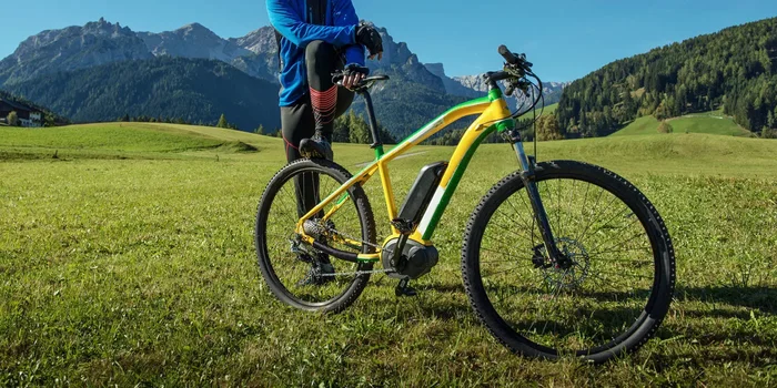 Radler lehnt an E-Mountainbike, im Hintergrund Berge