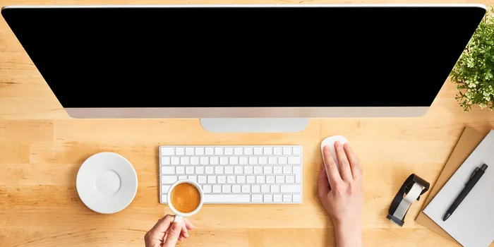 Draufsicht auf einen hölzernen Schreibtisch mit großem Desktop-Computer, Tastatur, Arbeitsmaterial und weiblichen Händen