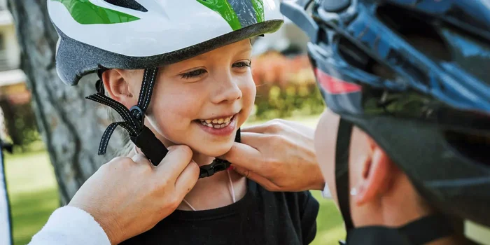Eine Frau hilft einem kleinen Jungen seinen Helm richtig aufzusetzen