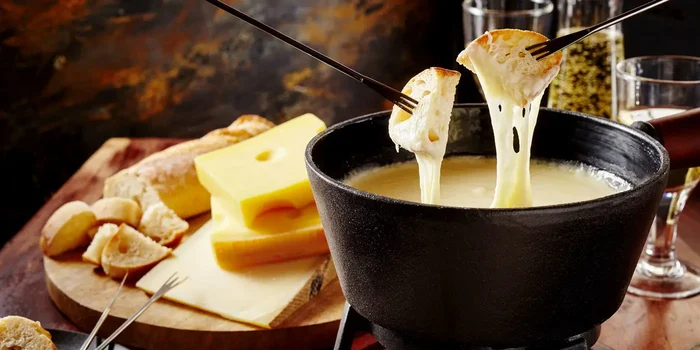 Weißbrot-Stücke werden in ein Käsefondue getunkt