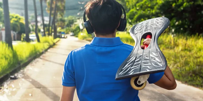 Person läuft mit Kopfhörern und Waveboard auf der Schulter die Straße herunter