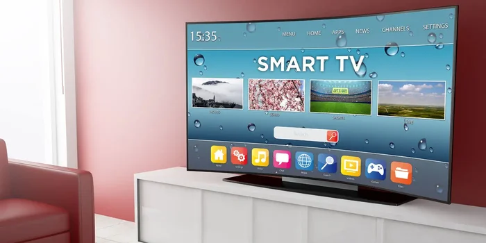 Großer Smart TV steht auf weißem Sideboard vor rötlicher Wand und neben rotem Ledersofa