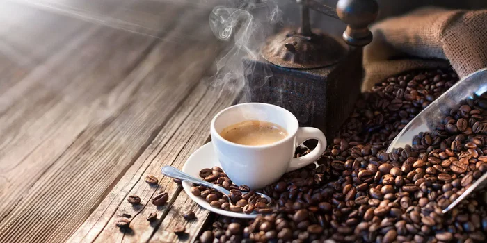 Kaffeebohnen neben einer Kaffeemühle und einer Tasse frisch aufgebrühtem Kaffee