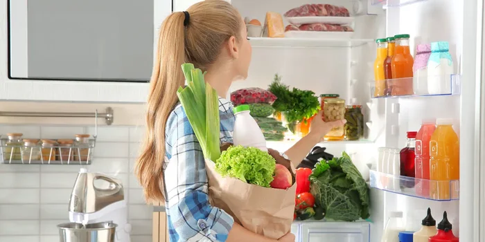 Frau räumt Einkäufe in den geöffneten Kühlschrank