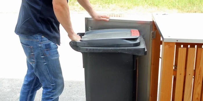 Mann entnimmt Mülltonne aus Mülltonnenbox aus Holz