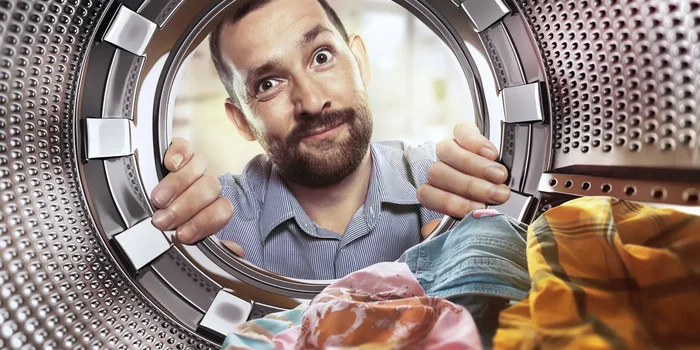 Mann mit Bart schaut fragend in die Trommel der Waschmaschine