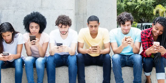 Sechs junge Menschen sitzen nebeneinander und haben jeweils ein Smartphone in der Hand