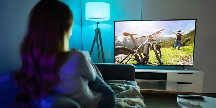 Frau entspannt auf Sofa in Wohnzimmer und schaut Fernsehen auf Flatscreen