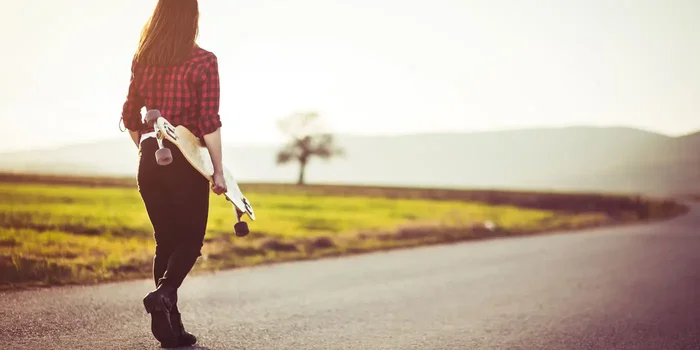 Frau mit Longboard in der Hand spaziert durch eine Landstrasse